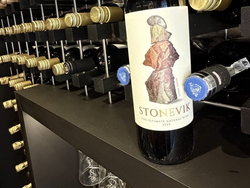 Garrafa de Stone Vik apoiada na prateleira da adega da Better Wine em Botafogo, com dezenas de garrafas deitadas no rack ao fundo