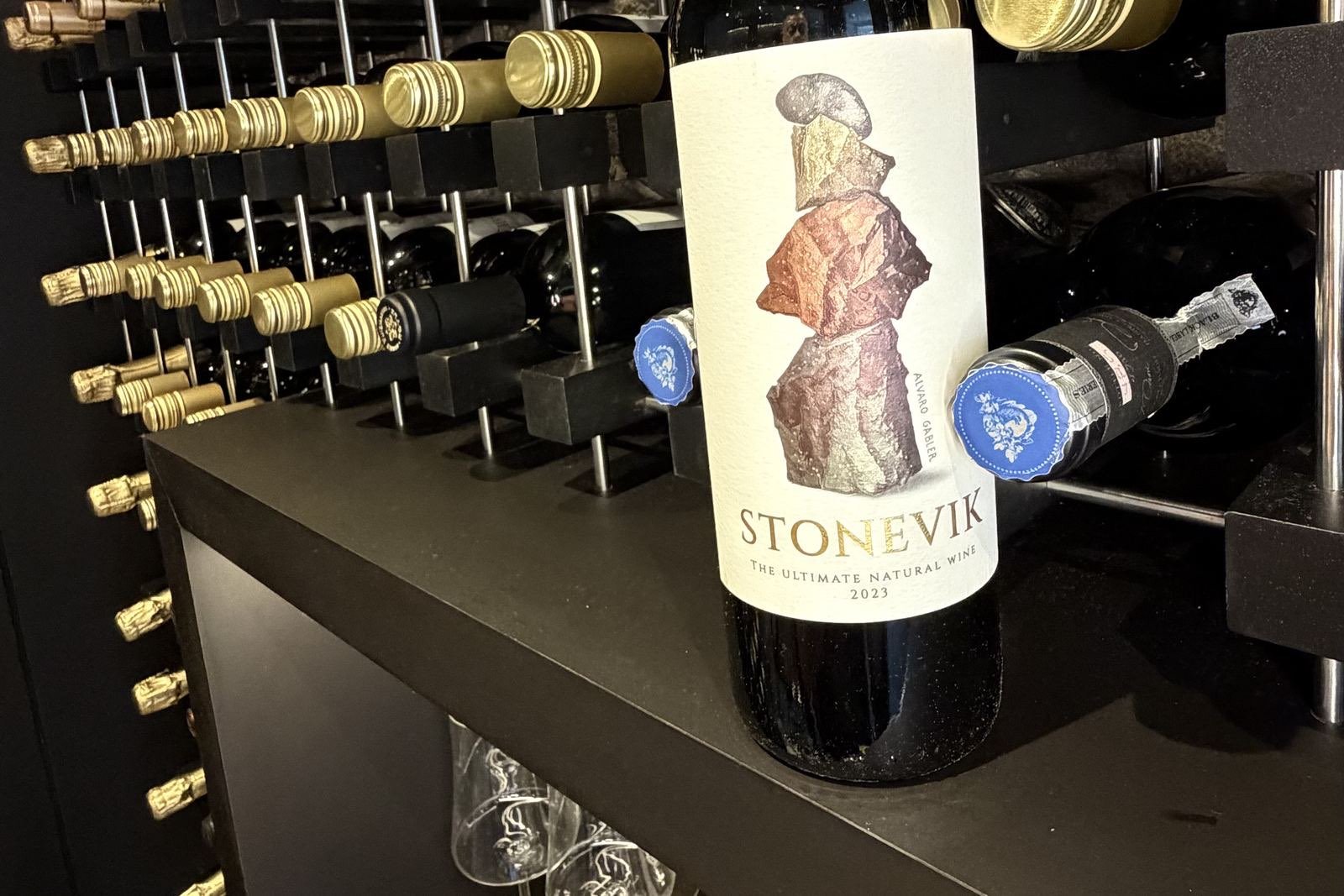 Garrafa de Stone Vik apoiada na prateleira da adega da Better Wine em Botafogo, com dezenas de garrafas deitadas no rack ao fundo