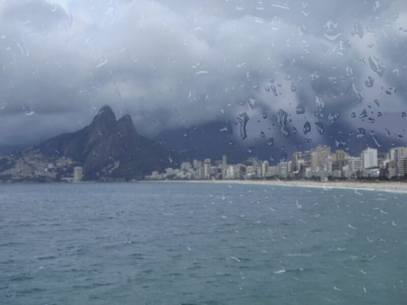 Morro Dois Irmãos e a praia de Ipanema vistos através de uma janela molhada de chuva, em dia frio e nublado no Rio de Janeiro
