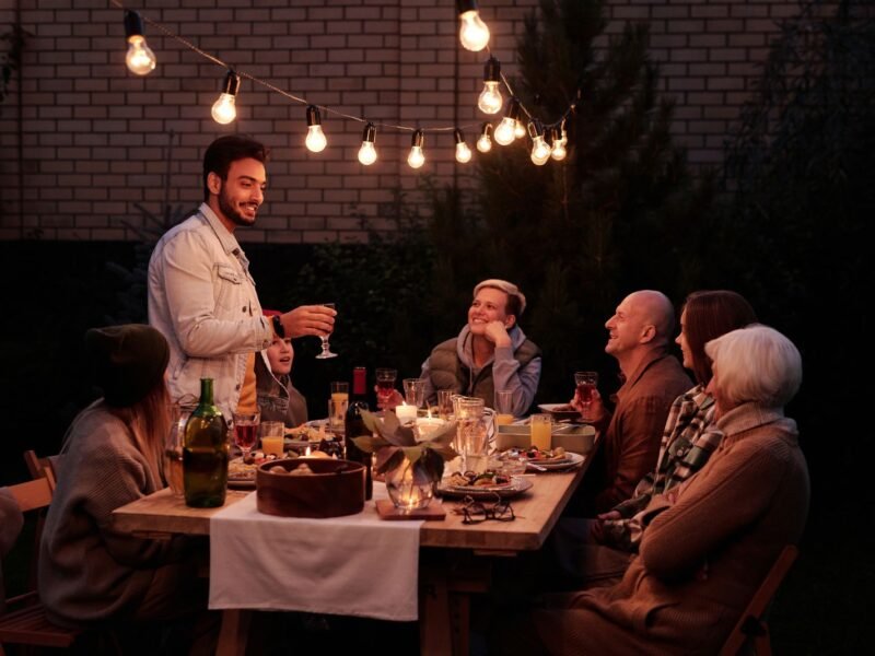 Família e amigos adultos reunidos em mesa ao ar livre com vinho, em uma confraternização de fim de semana
