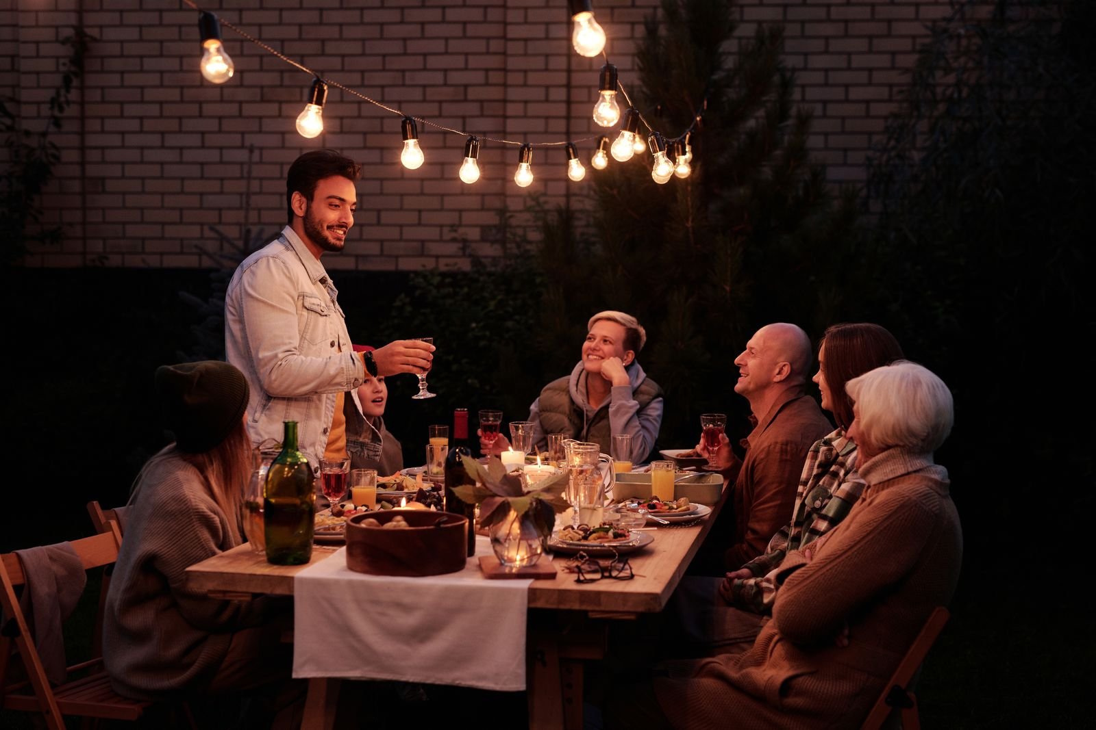 Família e amigos adultos reunidos em mesa ao ar livre com vinho, em uma confraternização de fim de semana