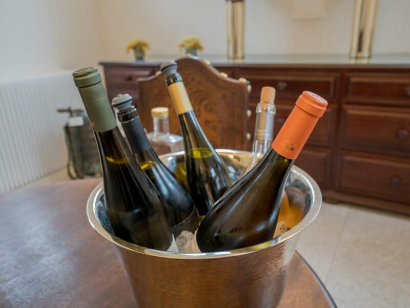 Garrafas de vinho branco e espumante gelando em balde de inox sobre mesa de madeira