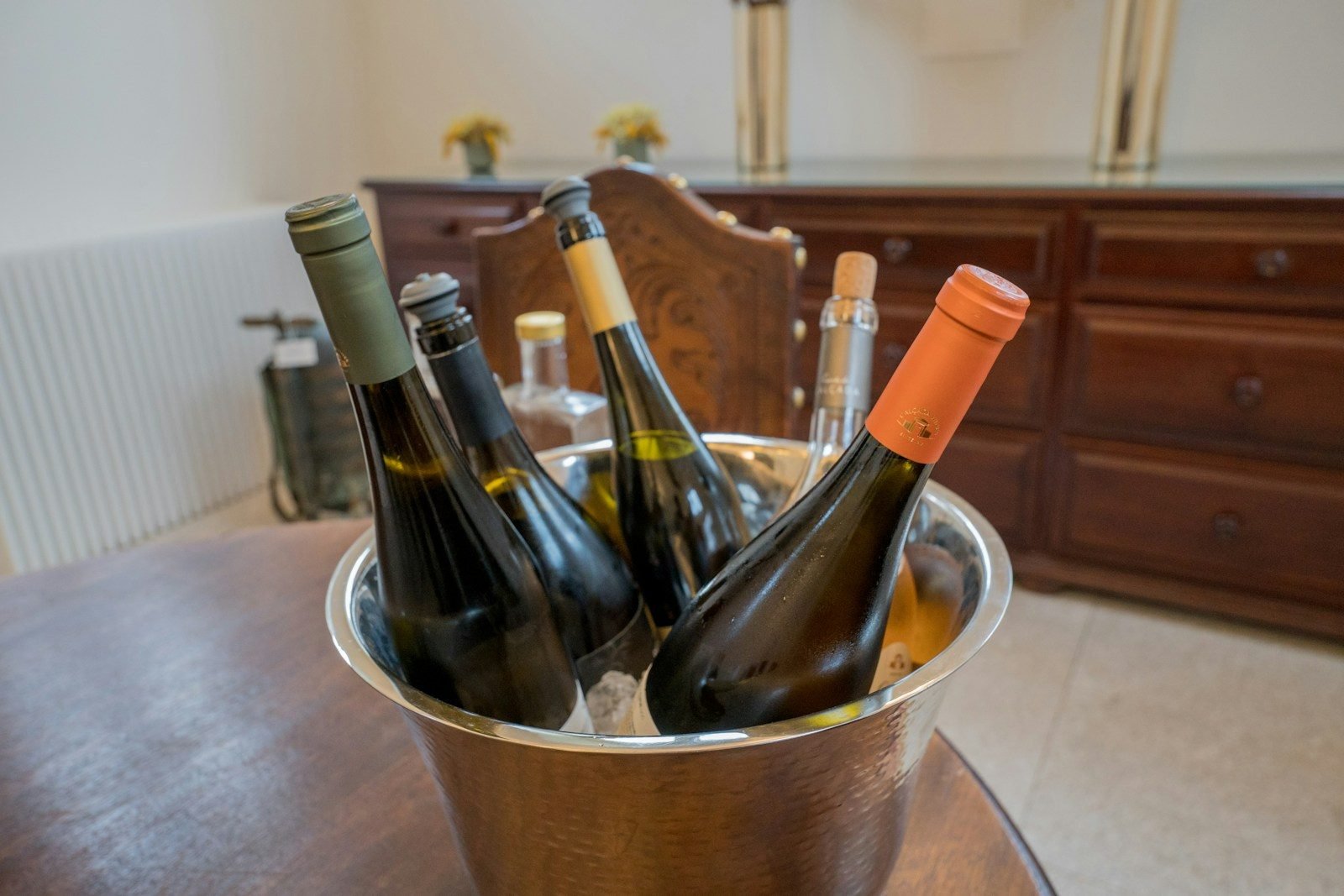 Garrafas de vinho branco e espumante gelando em balde de inox sobre mesa de madeira