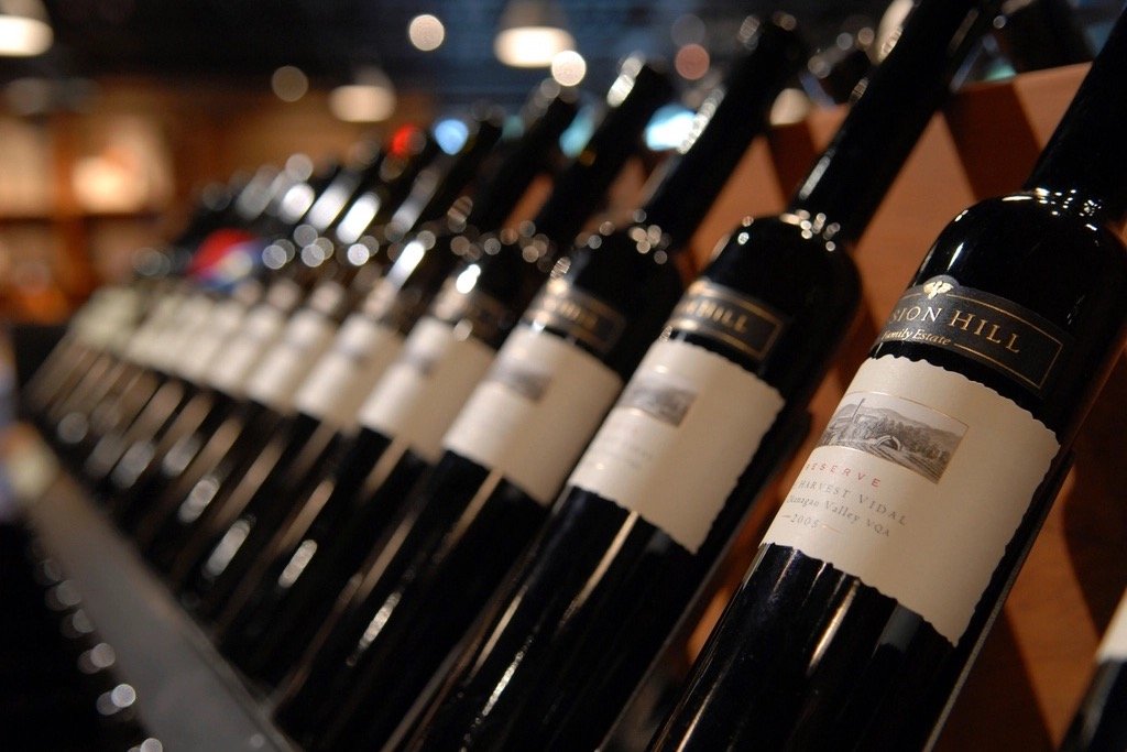 Fileira de garrafas de vinho tinto deitadas em prateleira de madeira de adega, com luz baixa ao fundo