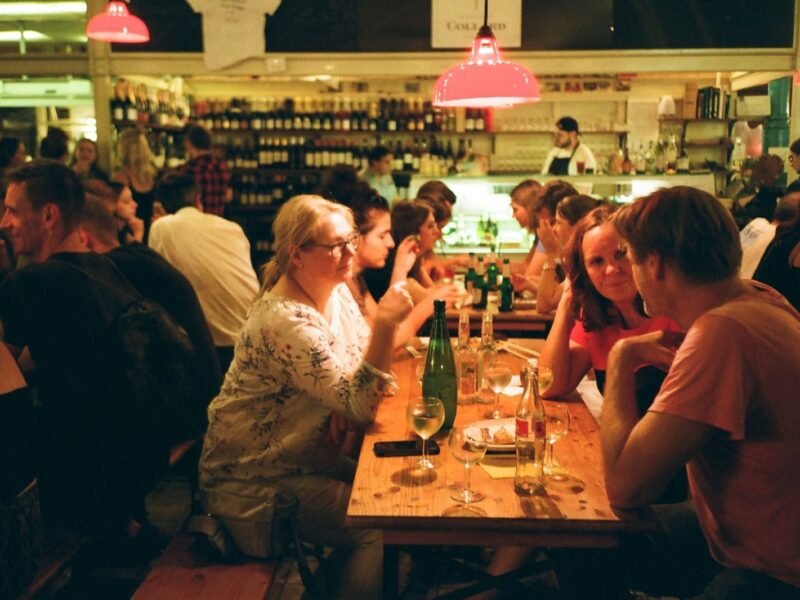 Mesa comunitária cheia de gente com garrafas e taças de vinho em um festival gastronômico