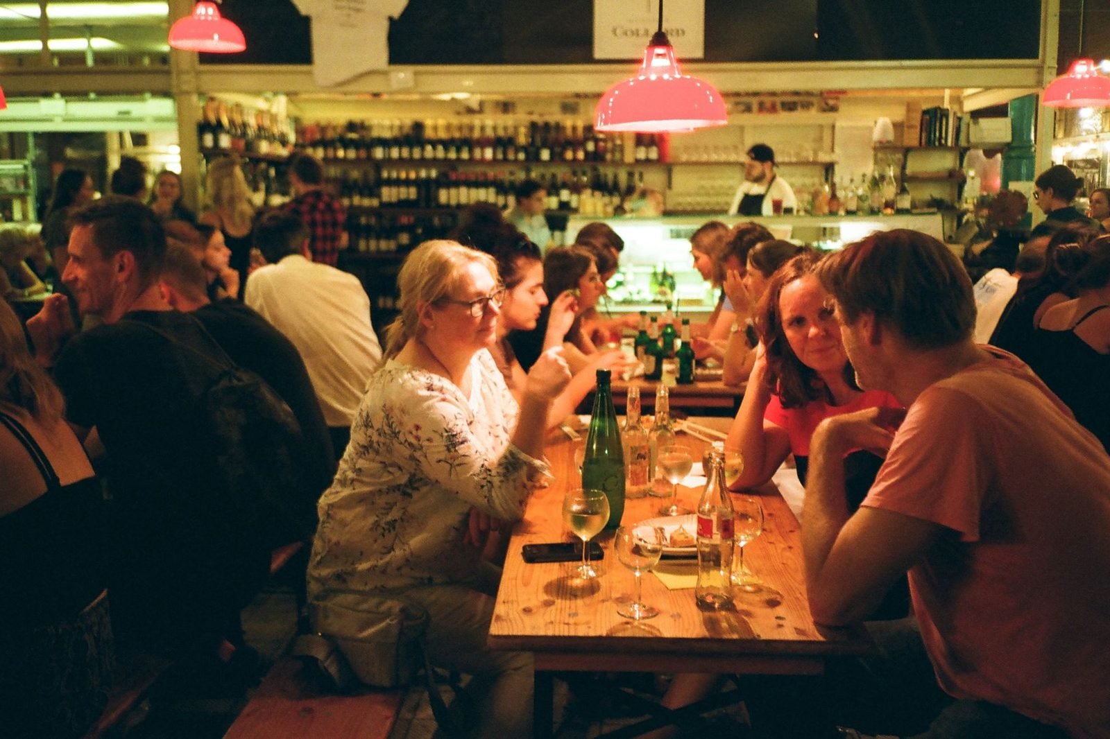 Mesa comunitária cheia de gente com garrafas e taças de vinho em um festival gastronômico