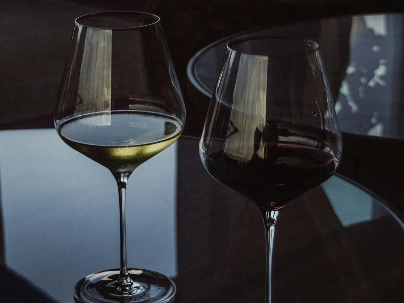 Uma taça de vinho branco e uma taça de vinho tinto lado a lado sobre mesa de vidro
