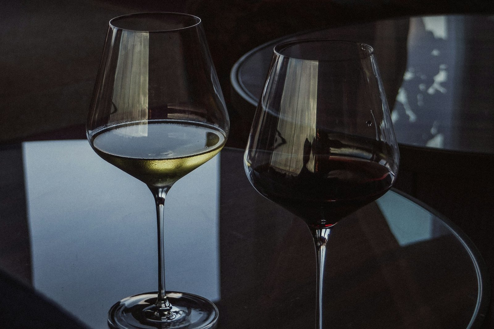 Uma taça de vinho branco e uma taça de vinho tinto lado a lado sobre mesa de vidro