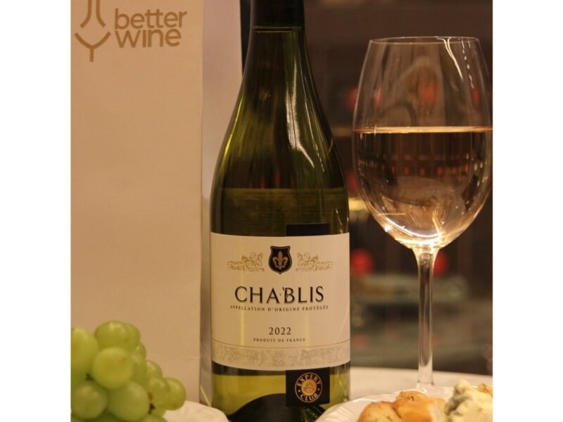 Garrafa de Chablis 2022 ao lado de uma taça de vinho branco, uvas verdes e queijo, com o logo da Better Wine ao fundo